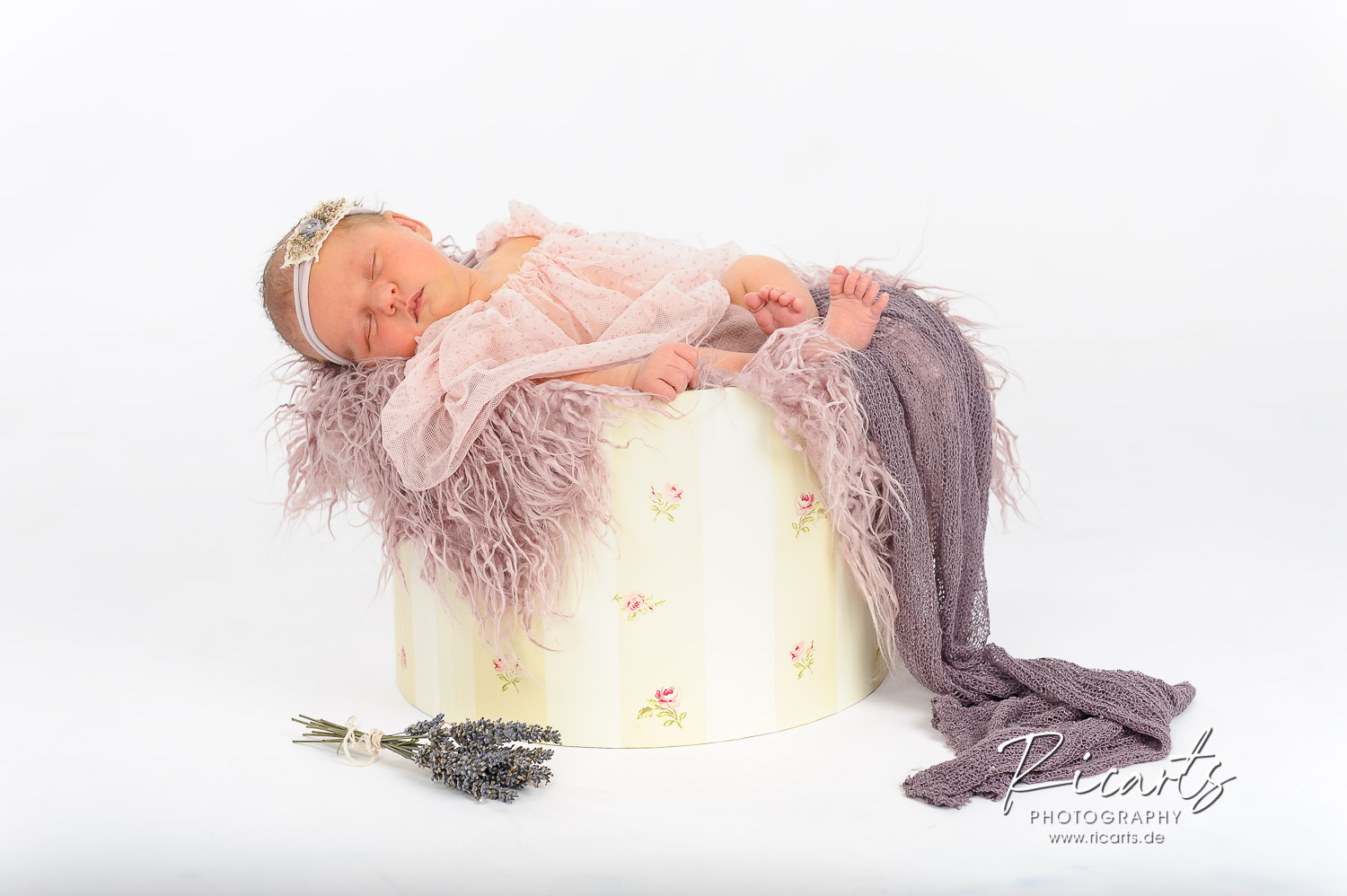 Newborn-Baby-liegt-schlafend-auf-rosafarbenem-Fell-in-einer-Blumen-Hutschachtel