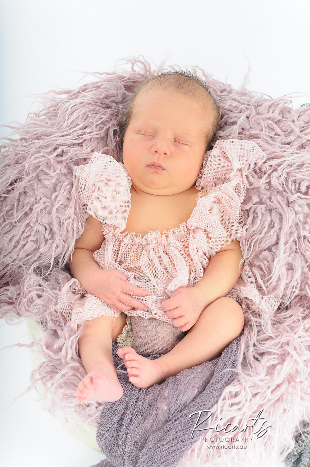 Newborn-Baby-liegt-schlafend-auf-rosafarbenem-Fell