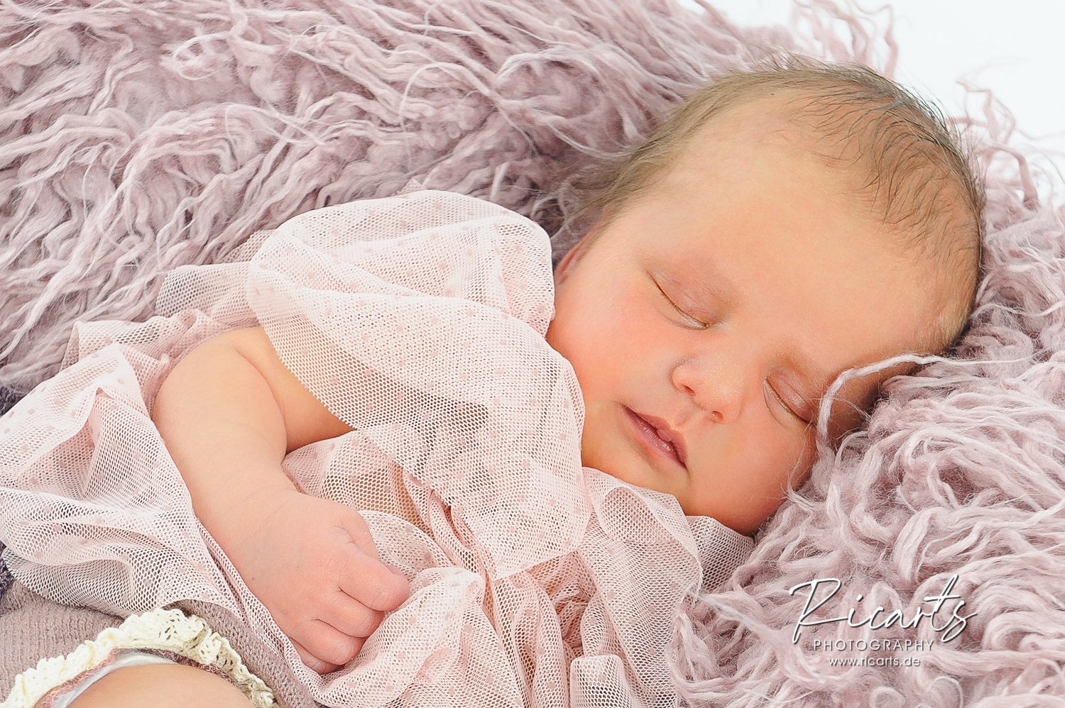 Newborn-Baby-liegt-schlafend-auf-rosafarbenem-Fell