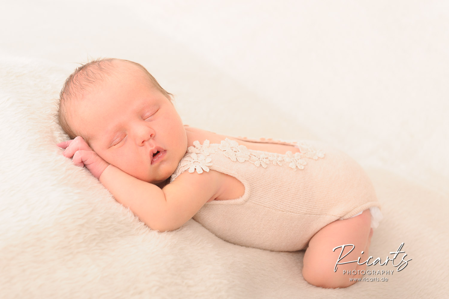 Newborn-Baby-liegt-schlafend-auf-cremefarbener-Decke