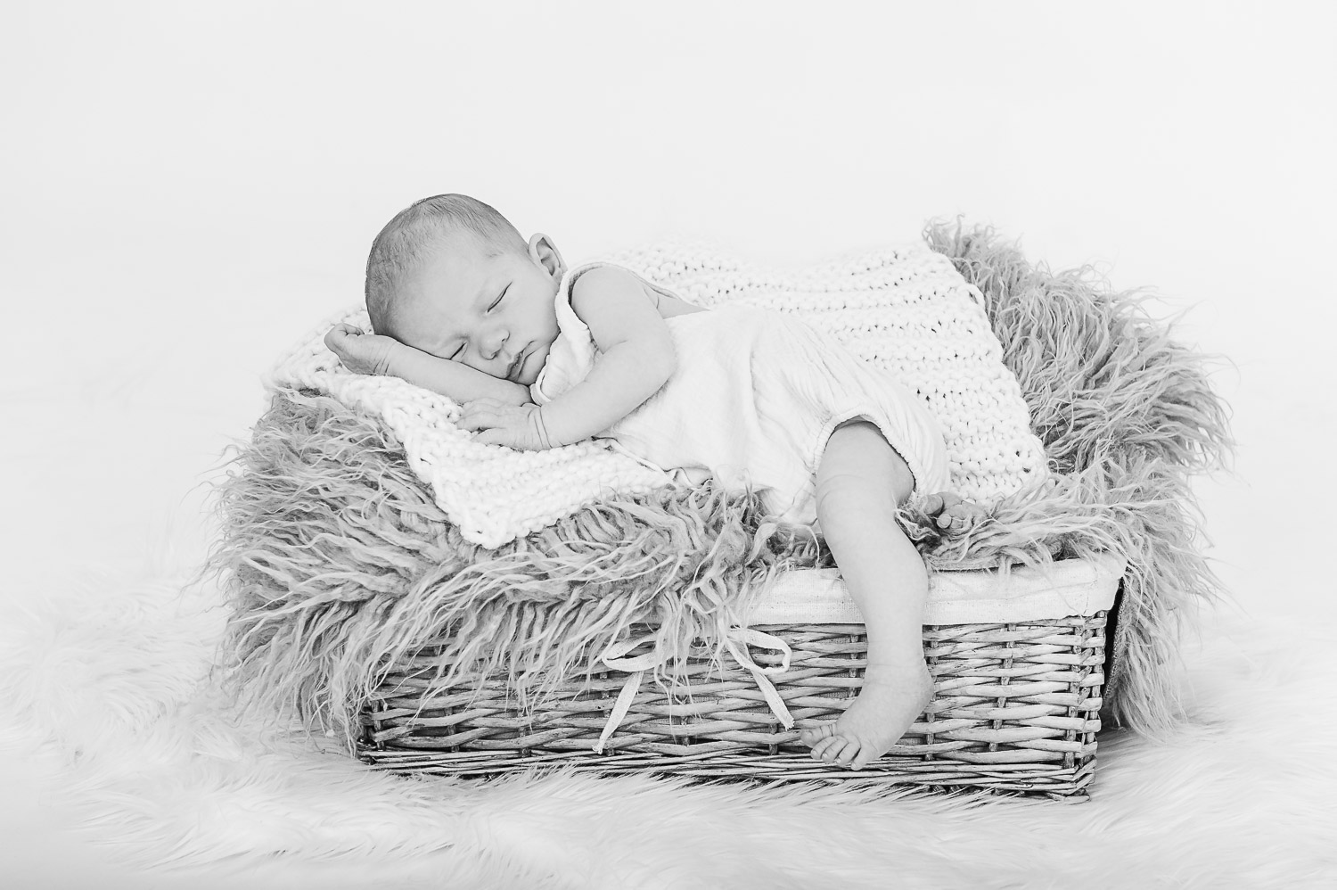 Newborn-Baby-liegt-schlafend-in-einem-Korb-und-hängt-das-Bein-über-den-Rand