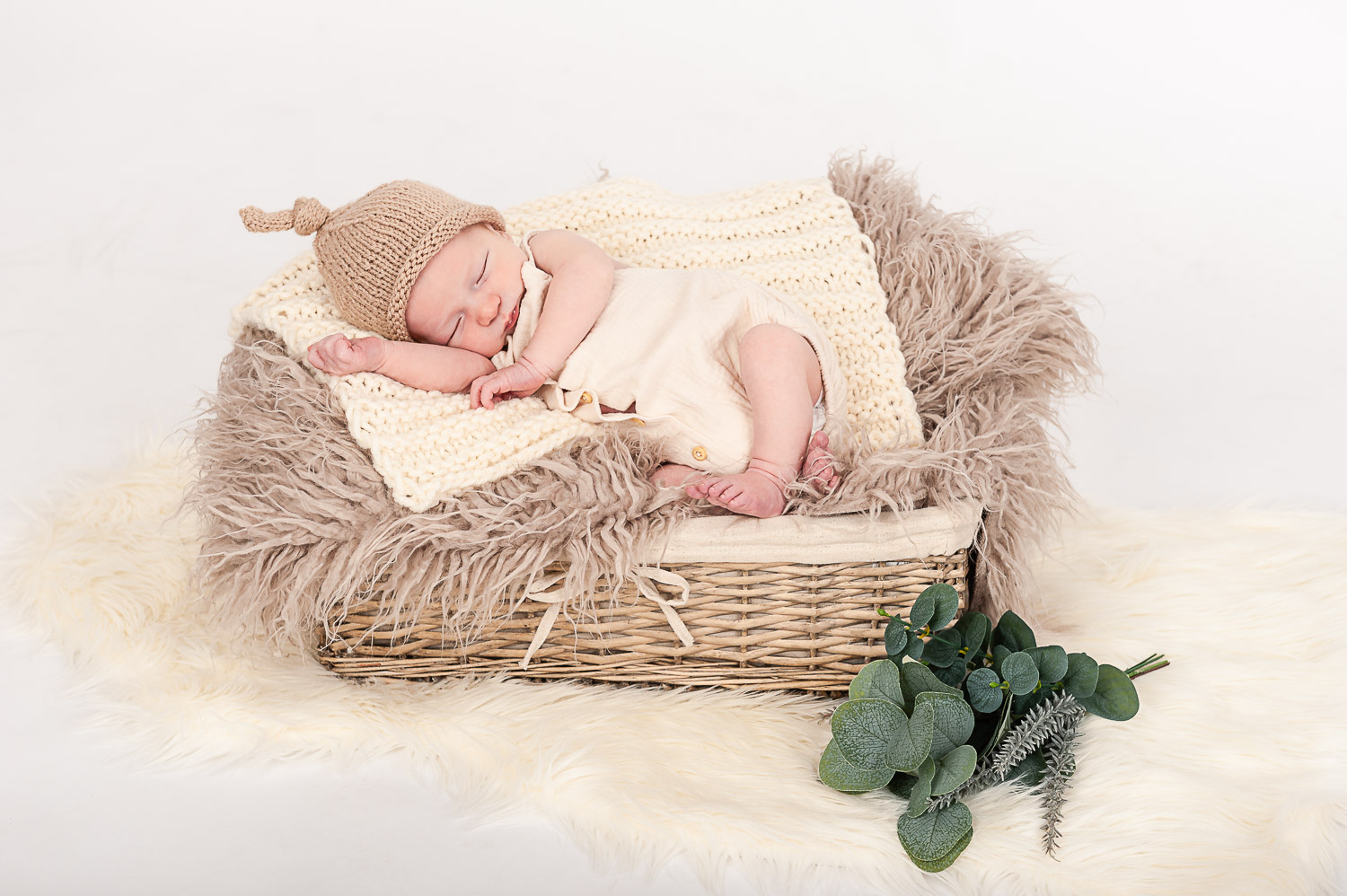 Newborn-Baby-liegt-schlafend-in-einem-Korb-mit-Strick-Mütze-und-Eukalyptuszweig