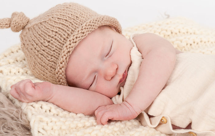 Newborn-Baby-mit-Strickmütze-liegt-schlafend-auf-beiger-Strickdecke