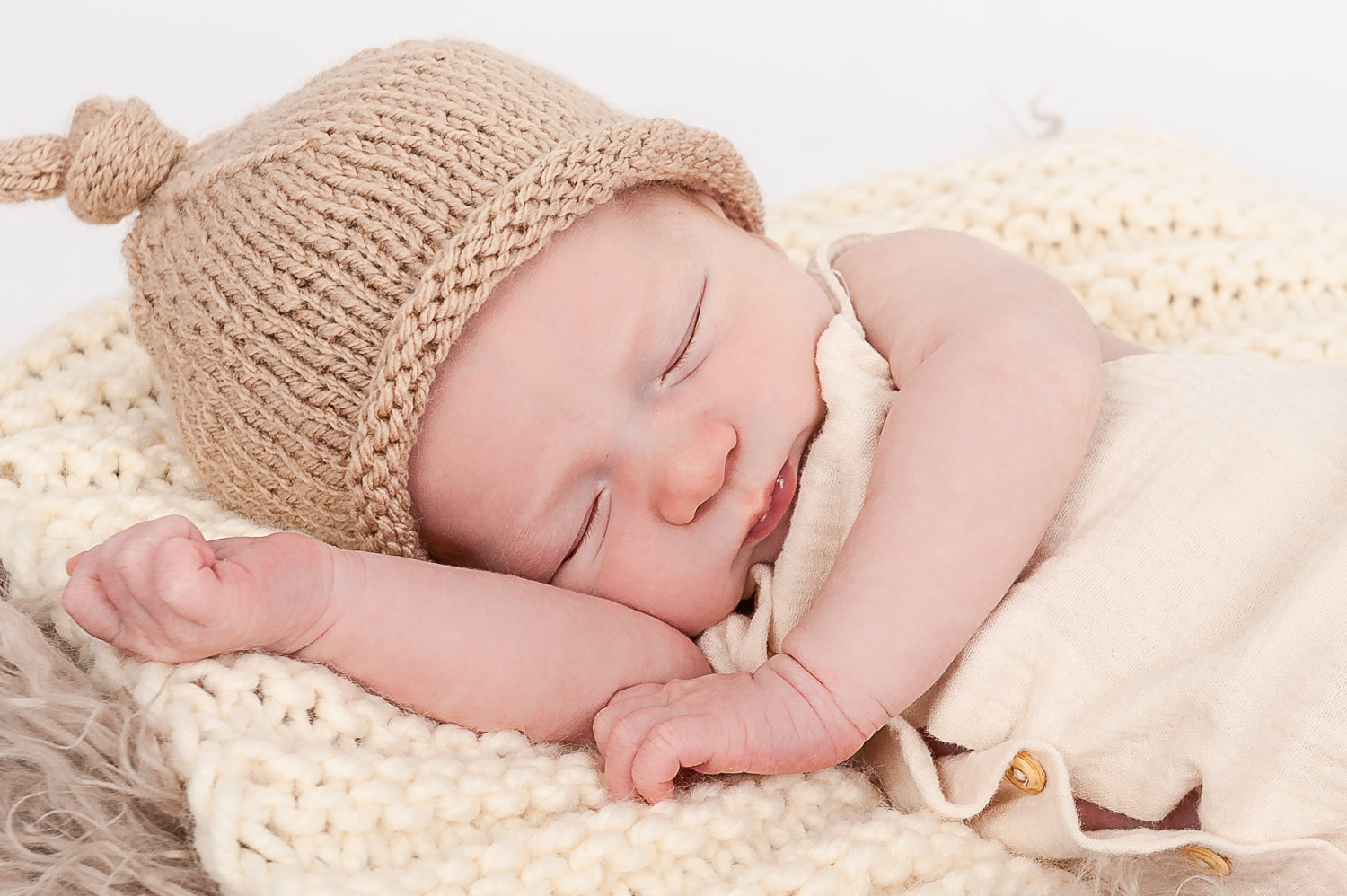 Newborn-Baby-mit-Strickmütze-liegt-schlafend-auf-beiger-Strickdecke