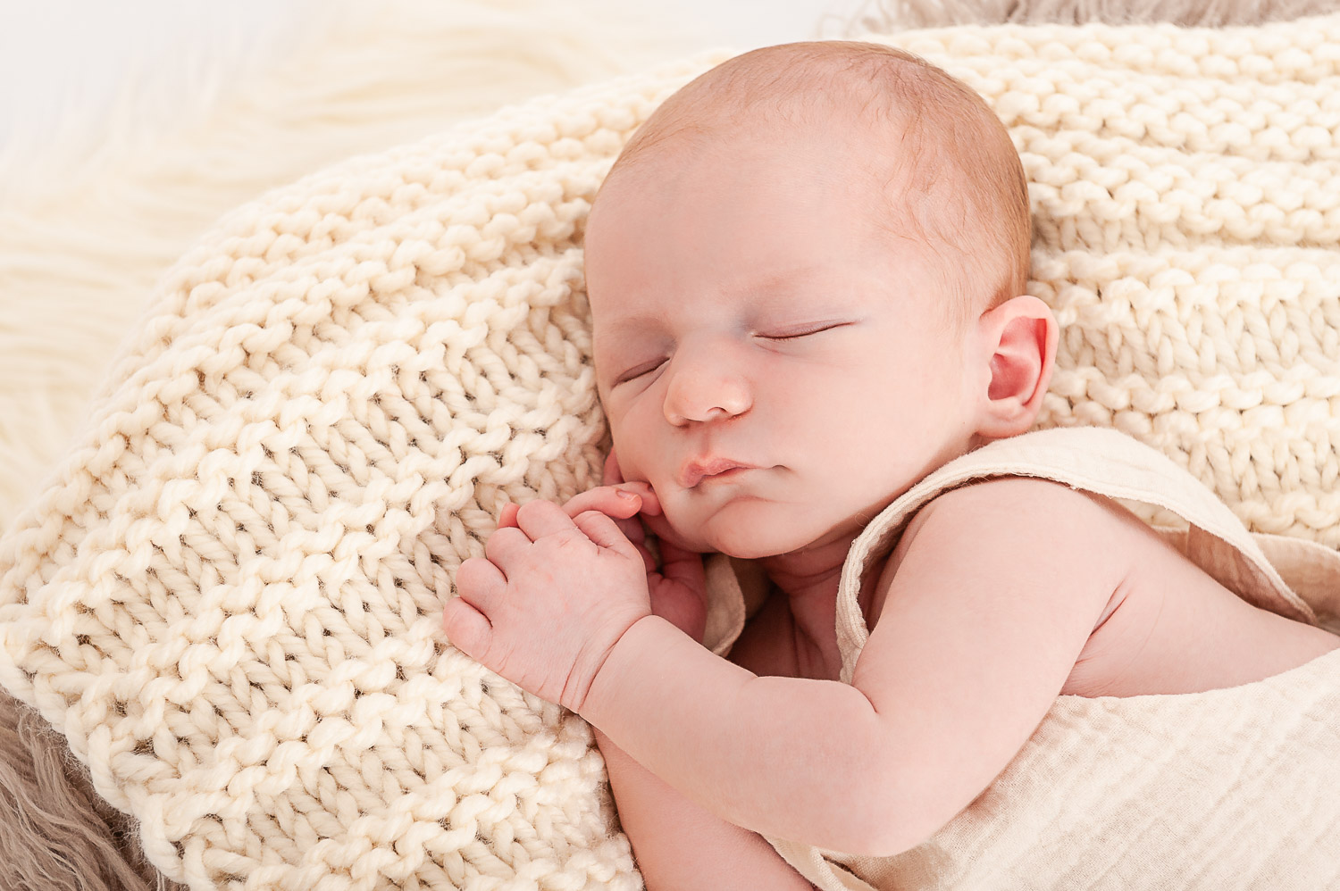 Newborn-Baby-liegt-schlafend-auf-beiger-Strickdecke