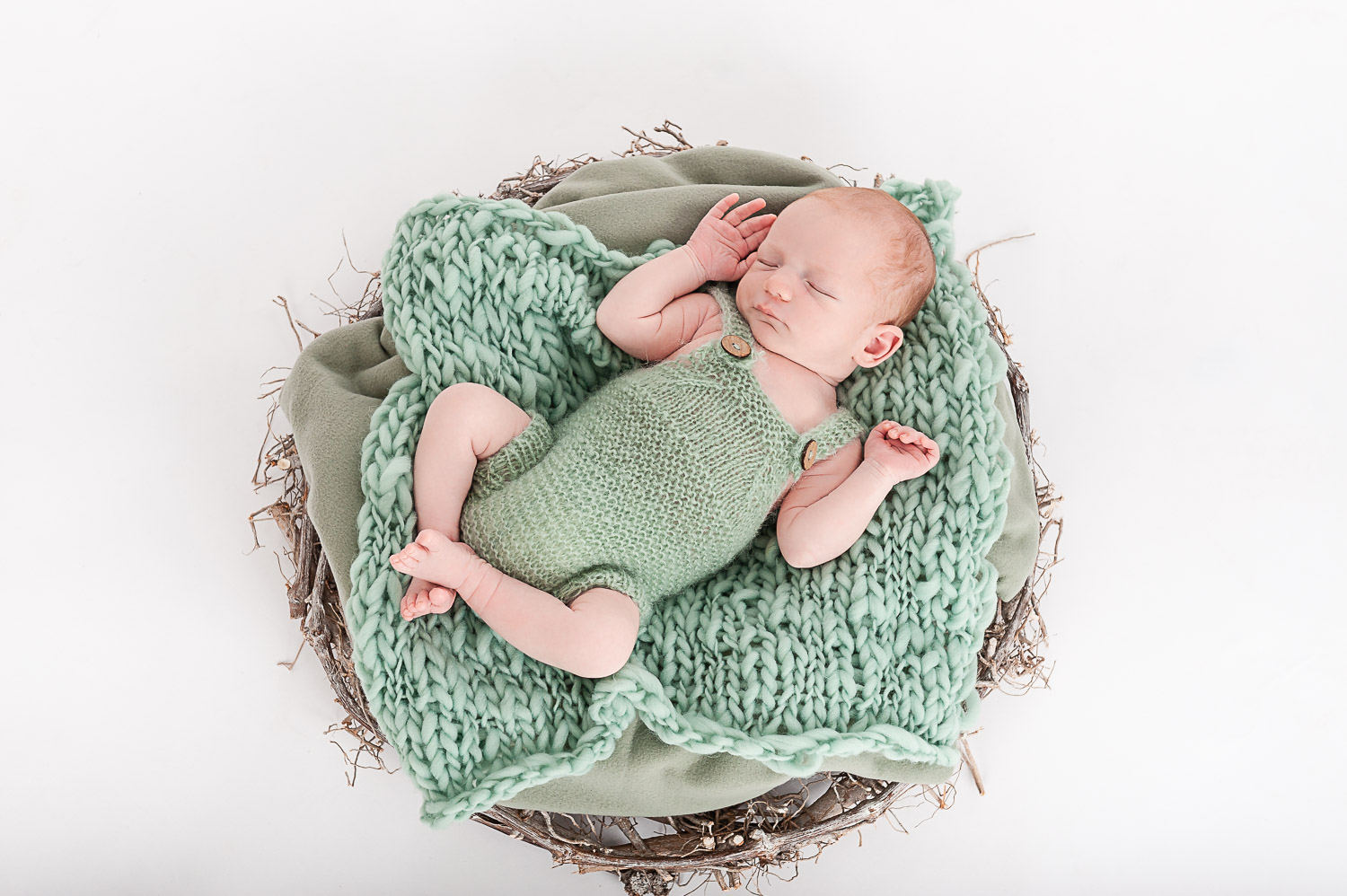 Newborn-Baby-liegt-auf-gruener-Strickdecke-auf-einem-Strohkranz