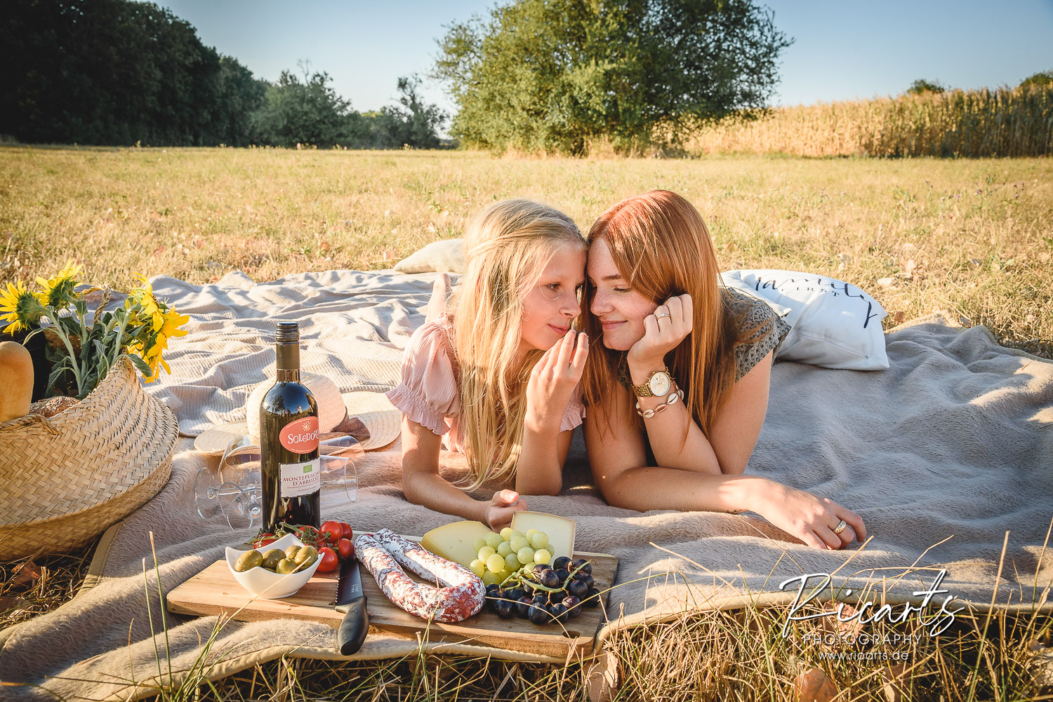 Familienfoto-Picknick-auf-Sommerwiese-zwei-Schwestern-liegen-auf-Picknickdecke