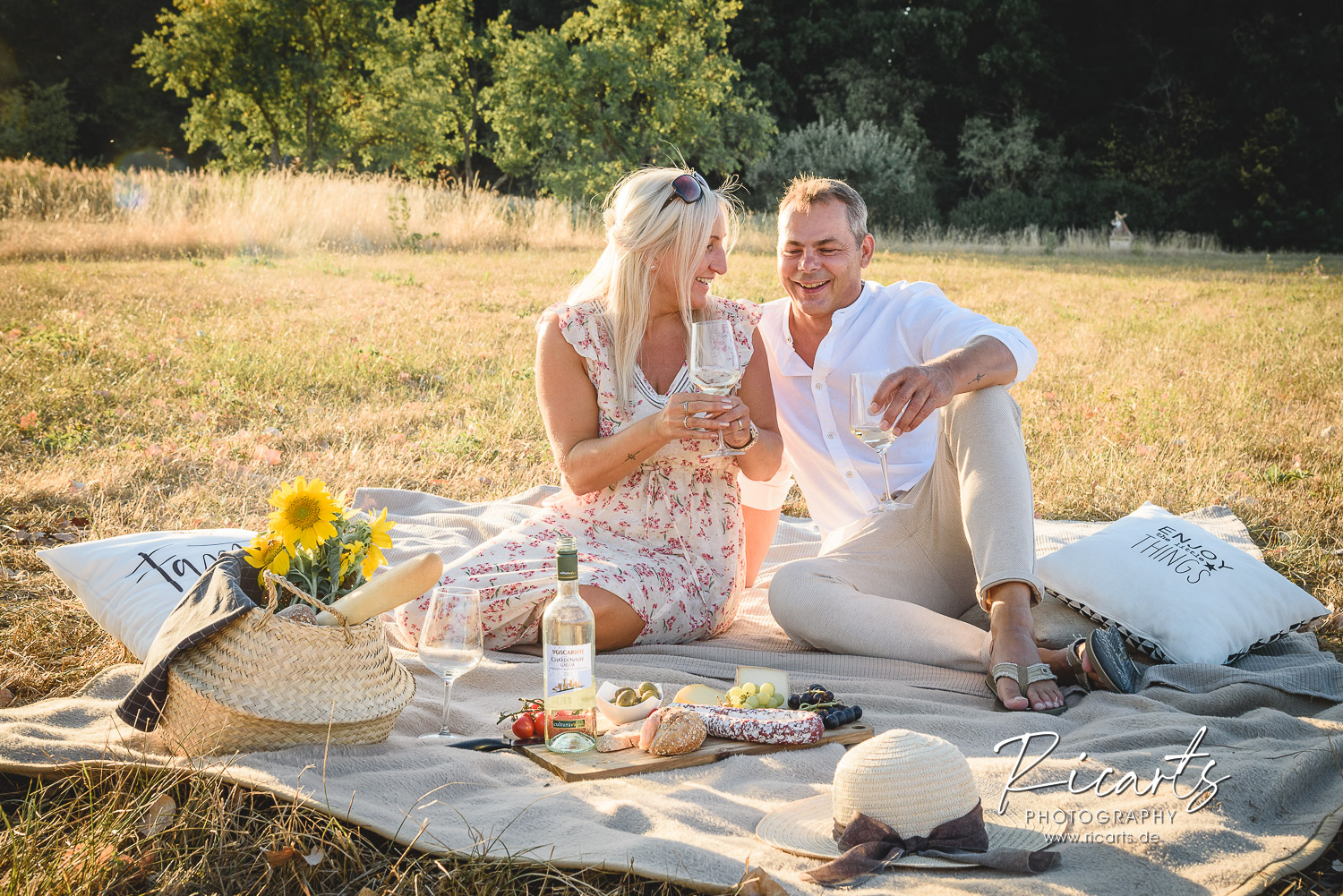 Paar-sitzt-auf-Picknickdecke-in-der-Abendsonne-mit-einem-Glas-Wein