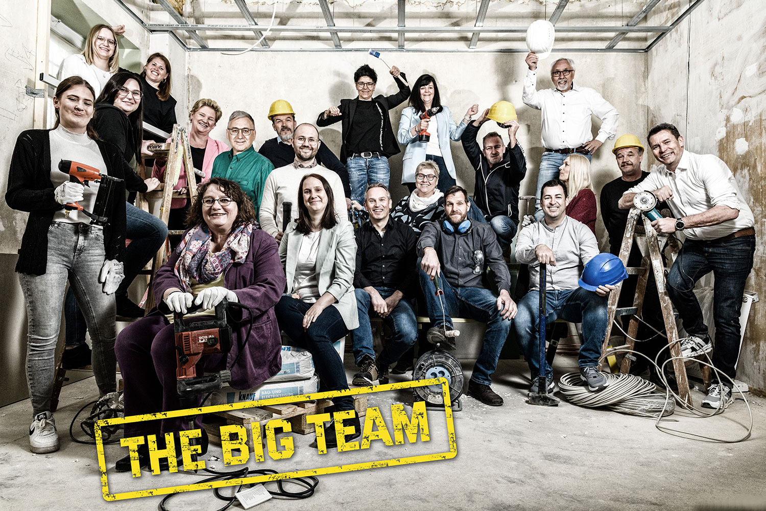 Gruppenfoto-Mitarbeiter-einer-Firma-stehen-und-sitzen-auf-einer-Baustelle-mit-Helmen-oder-Geräten-in-der-Hand