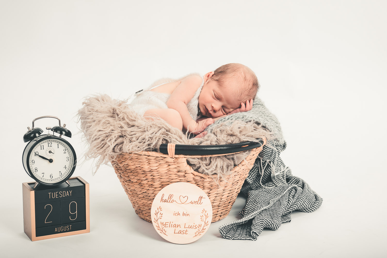 Newborn-Baby-liegt-schlafend-in-einem-Korb-mit-Deko-Wecker-und-Datums-Würfel