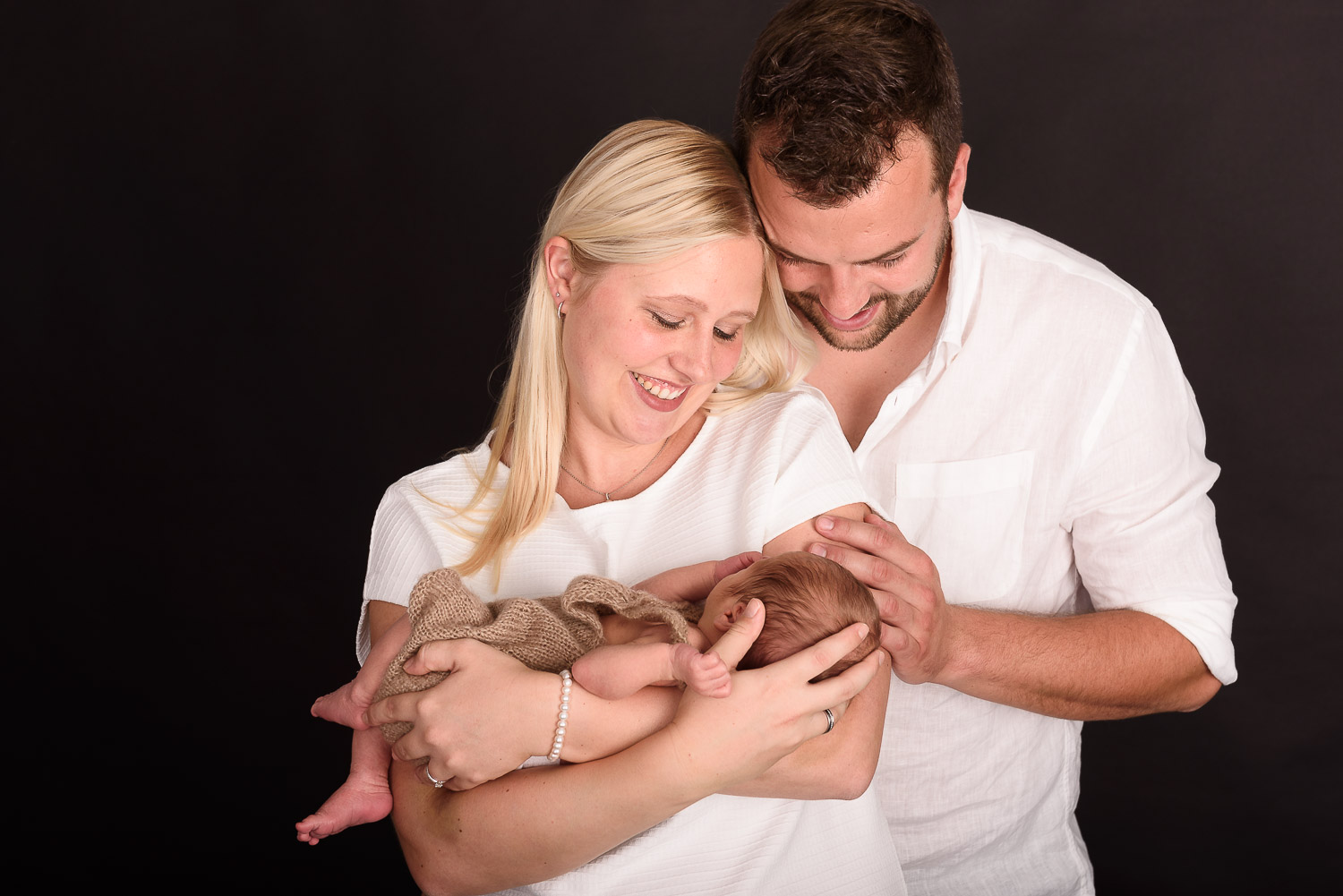 Junges-Elternpaar-hält-Newbornbaby-auf-dem-Arm-und-schaut-es-an