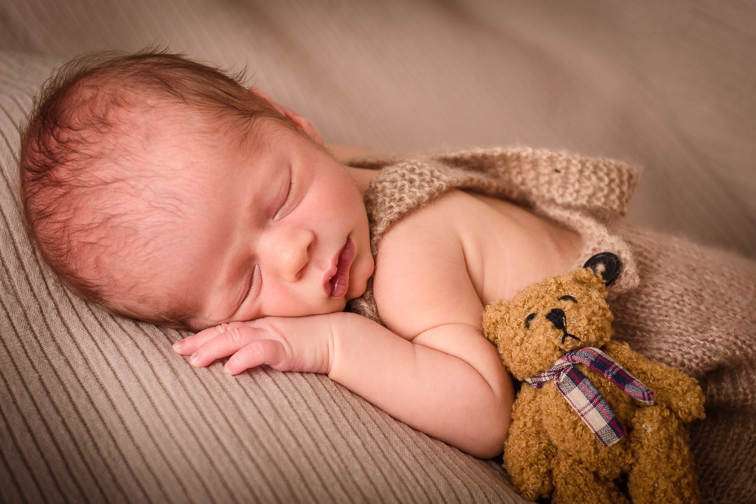 Newborn-Baby-liegt-schlafend-auf-dem-Bauch-mit-einem-kleinen-Teddybaer