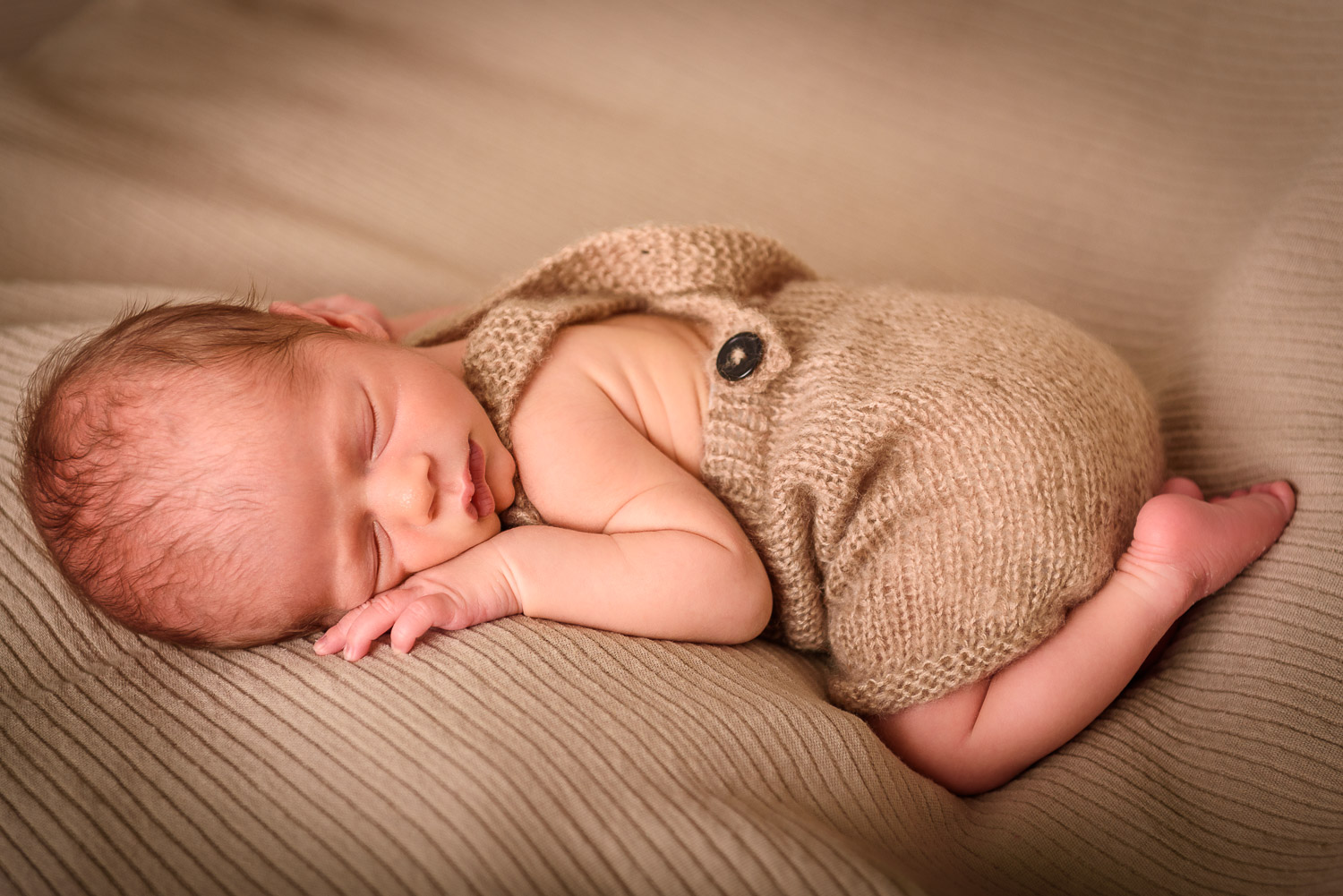 Newborn-Baby-liegt-schlafend-auf-dem-Bauch-mit-angezogenen-Beinen