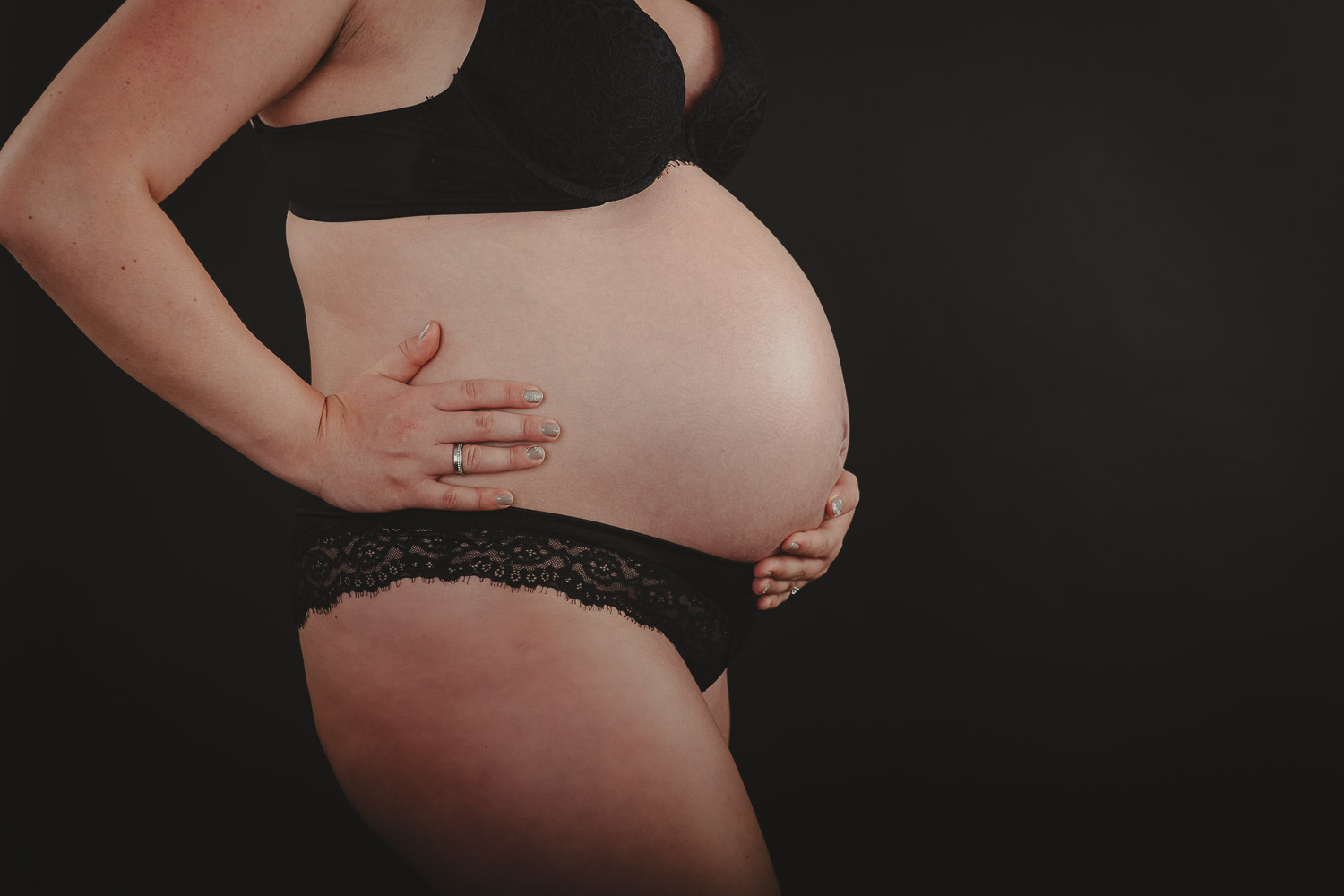 Schwangere-Frau-in-Unterwaesche-vor-dunklem-Hintergrund
