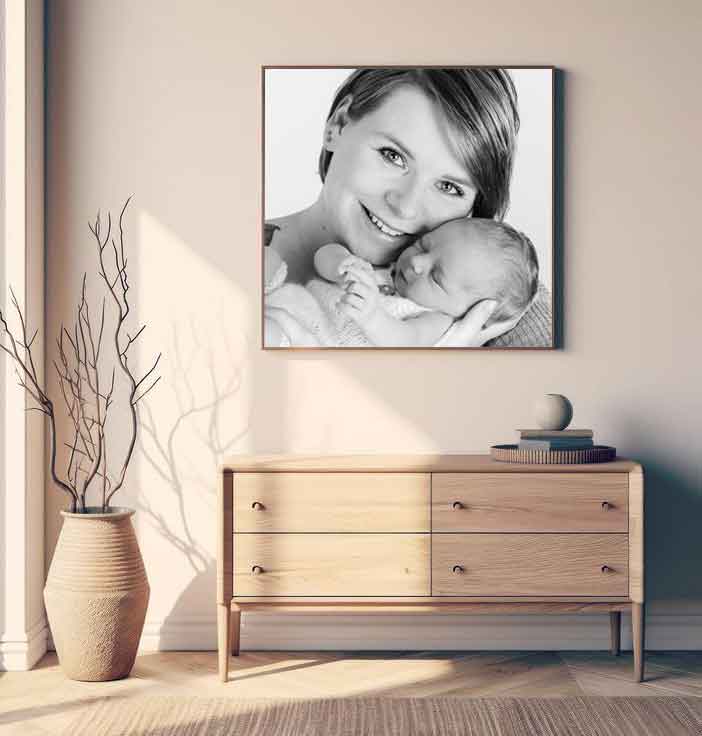 Bilder einer Mutter die ihr Newborn Baby im Arm hält hängt über einer Holzkommode