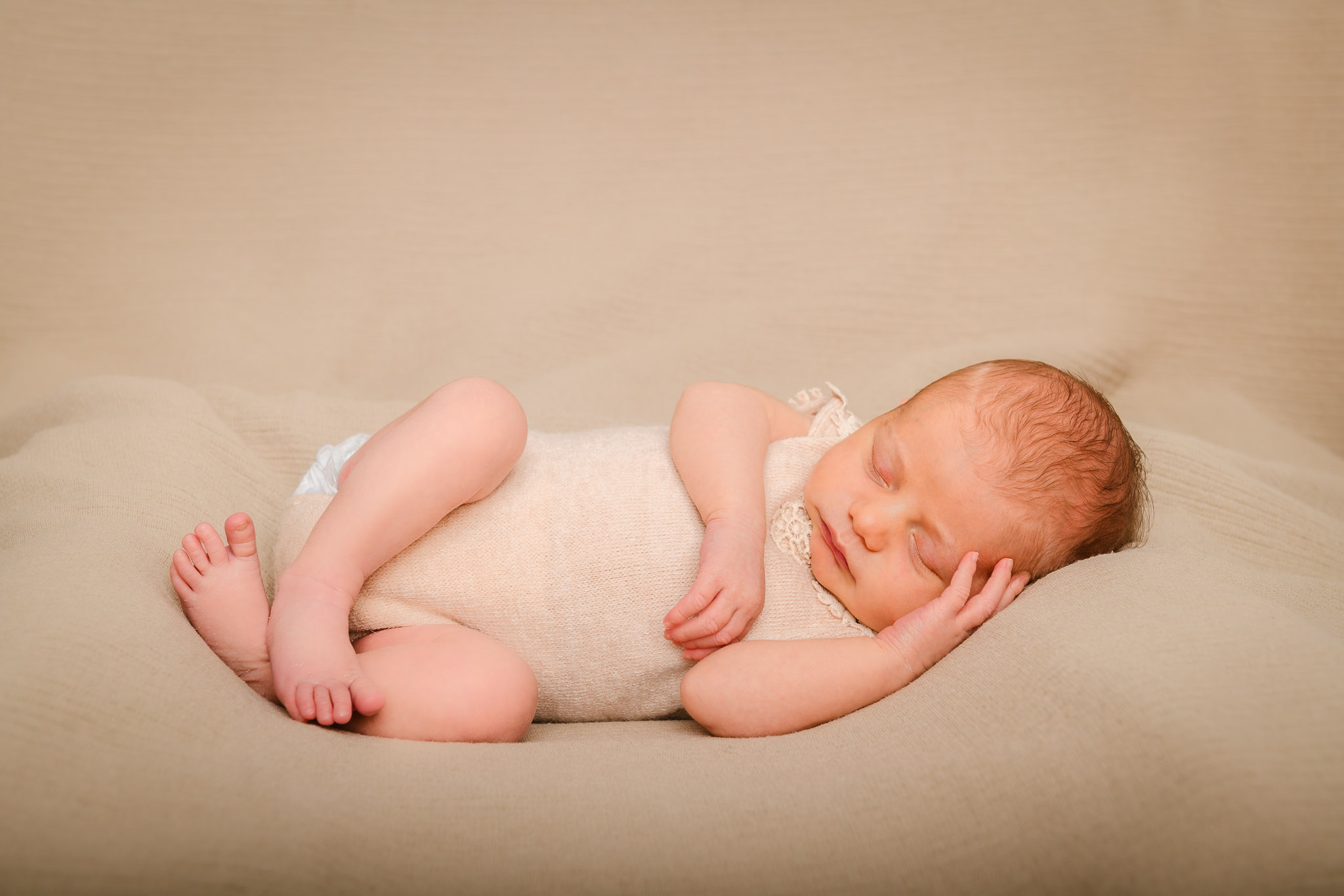 neugeborenes Baby liegt schlafend auf einem beigefarbenem Kissen