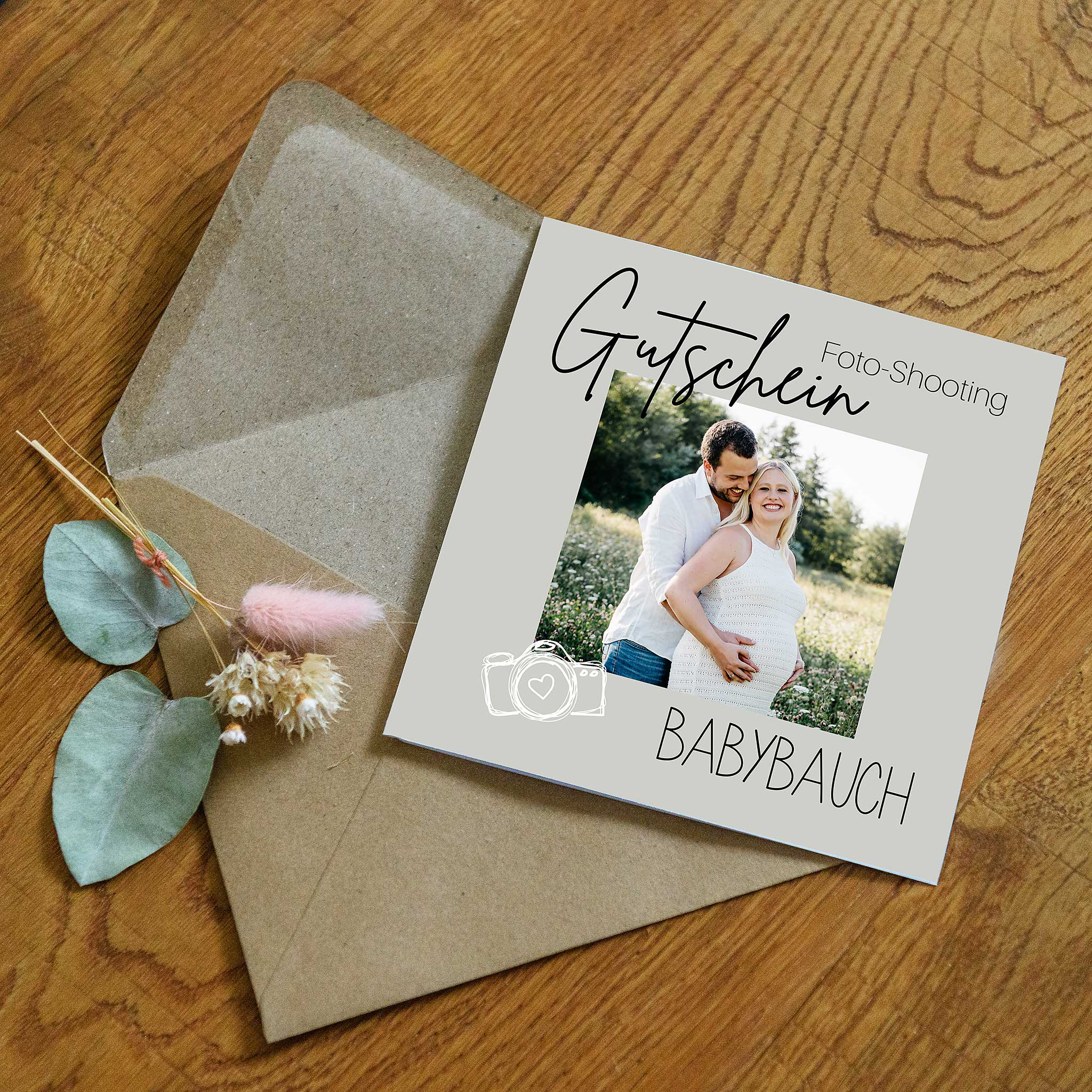 quadratischer Gutschein für ein Fotoshooting mit einem Umschlag und Deko auf Holzhintergrund